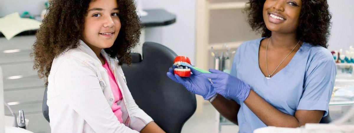 Young girl at a UAE dental clinic learning about teeth from a friendly dentist holding a tooth model